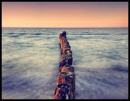 Leinwandbild von einem hölzernen Wellenbrecher der in das Meer hinein ragt.