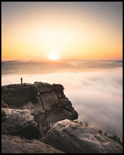 Ein Poster von einem Bergsteiger, der bei Sonnenaufgang auf einer Klippe steht.