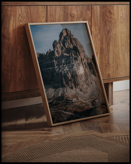 Ein gerahmtes Poster von einem massiven Berg in den Dolomiten, an einer Holzkommode angelehnt und stehend auf dem Holzboden