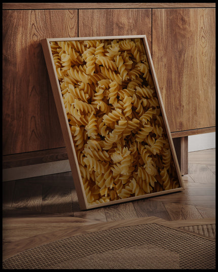 Ein gerahmtes Poster von vielen Fusilli Nudeln, an einer Holzkommode angelehnt und stehend auf dem Holzboden