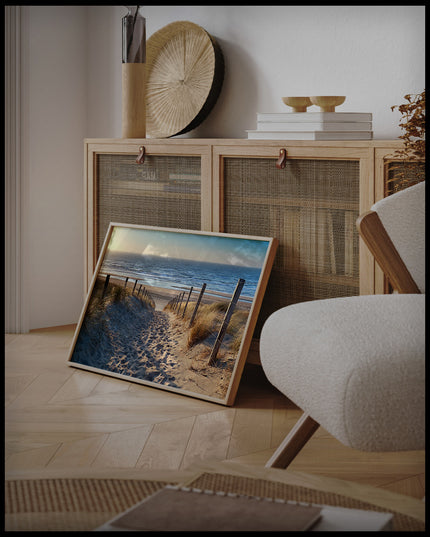 Ein gerahmtes Poster von Fußspuren im Sand auf einem Sandweg zum Strand, an einer Holzkommode angelehnt und stehend auf dem Holzboden