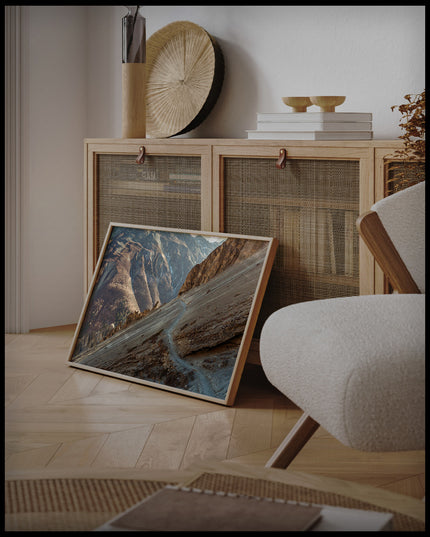 Ein gerahmtes Poster von einem Wanderweg in einer kargen, trockenen Berglandschaft, an einer Holzkommode angelehnt und stehend auf dem Holzboden