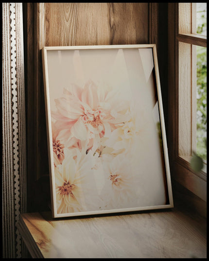 Ein gerahmtes Poster von zarten, pastellfarbenen Dahlienblüten, vor einem Fenster an die Wand angelehnt