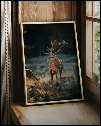 Ein gerahmtes Poster von einem majestätischen Hirsch mit großem Geweih in einer herbstlichen Landschaft, vor einem Fenster an die Wand angelehnt