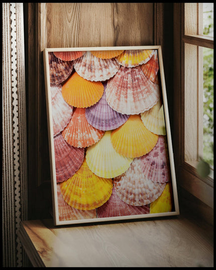 Ein gerahmtes Poster einer Nahaufnahme von bunten Muscheln die nebeneinander und übereinander angeordnet sind, vor einem Fenster an die Wand angelehnt