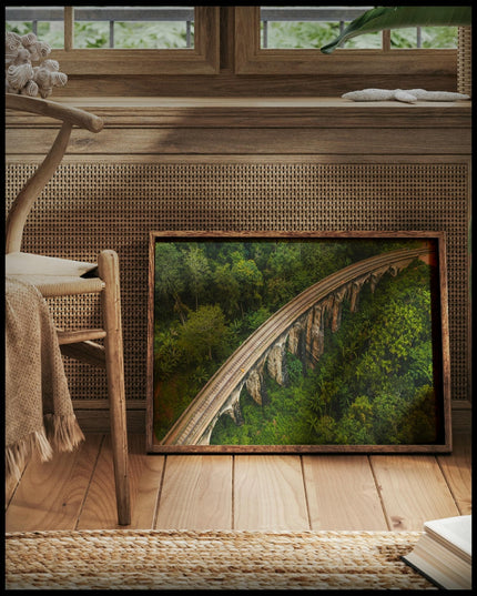 Ein gerahmtes Poster aus der Vogelperspektive von einer Viaduktbrücke aus Stein die durch einen tropischen Wald führt, vor einem Fenster an die Wand angelehnt