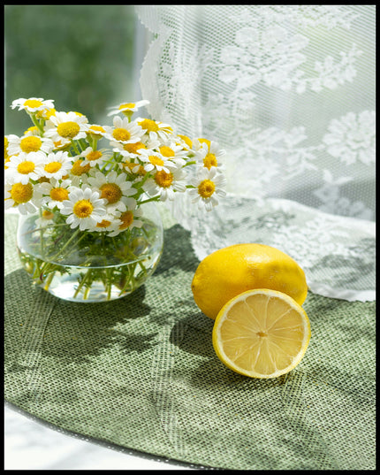 Ein Poster von zwei Zitronen und Blumen in einem Glas auf einer grünen Unterlage aus Stoff.